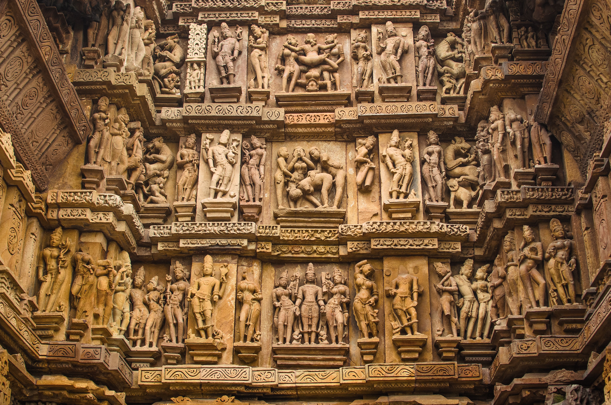 An interior wall of a temple is heavily adorned with intricate stone carvings of Hindu deities, animals and figures in sexual union, separated by bands of decoration.