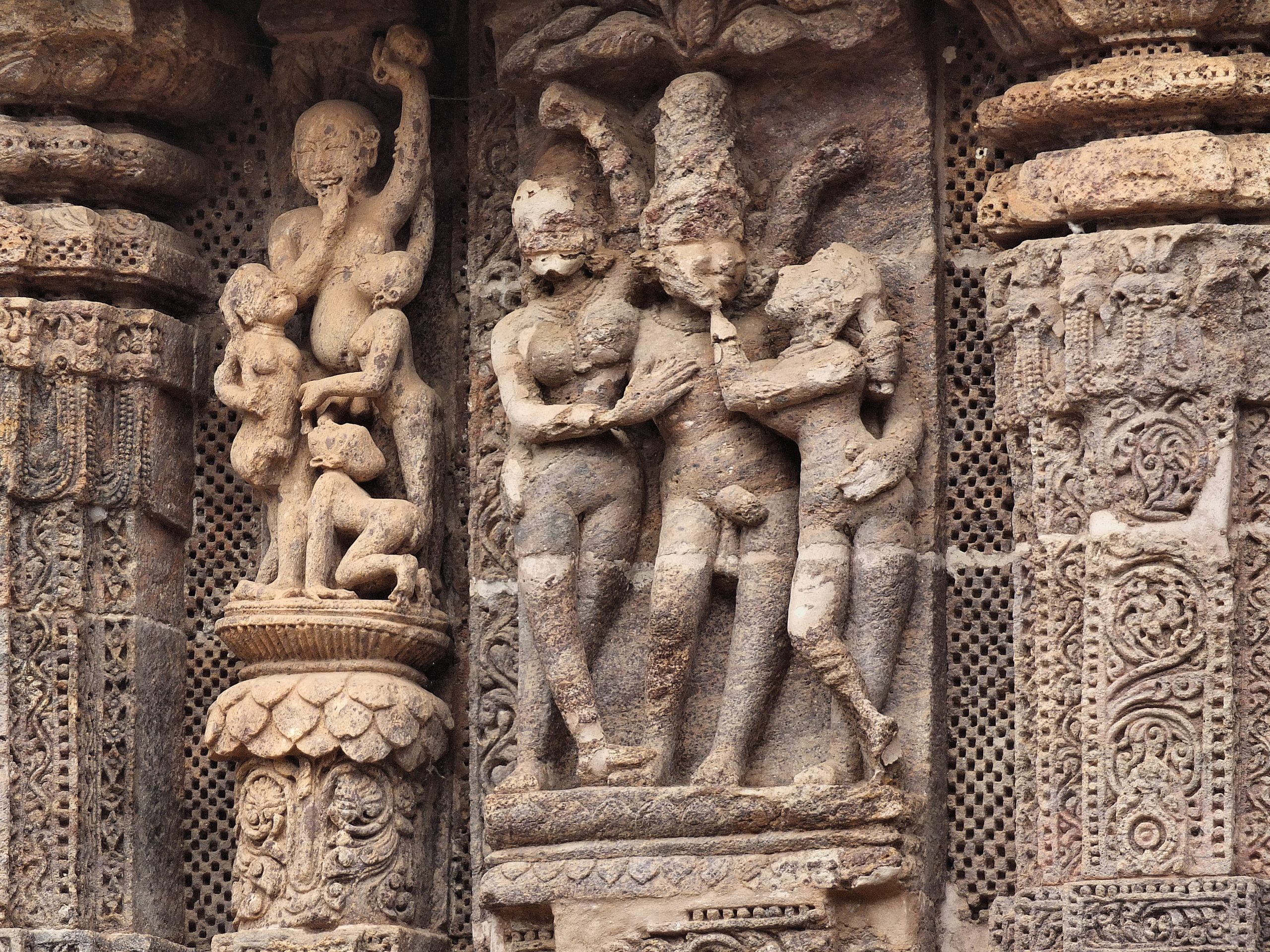 Two stone carvings of figures in sexual union in the niches of a wall featuring floral and chequered patterns.