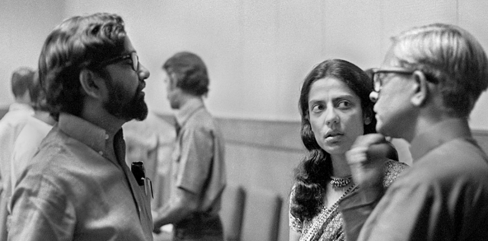 Two men and a woman engage in conversation while facing each other in a room.