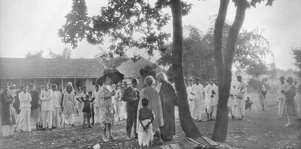 A large group of students surround a bearded man in conversation with a European man and woman outside a building.