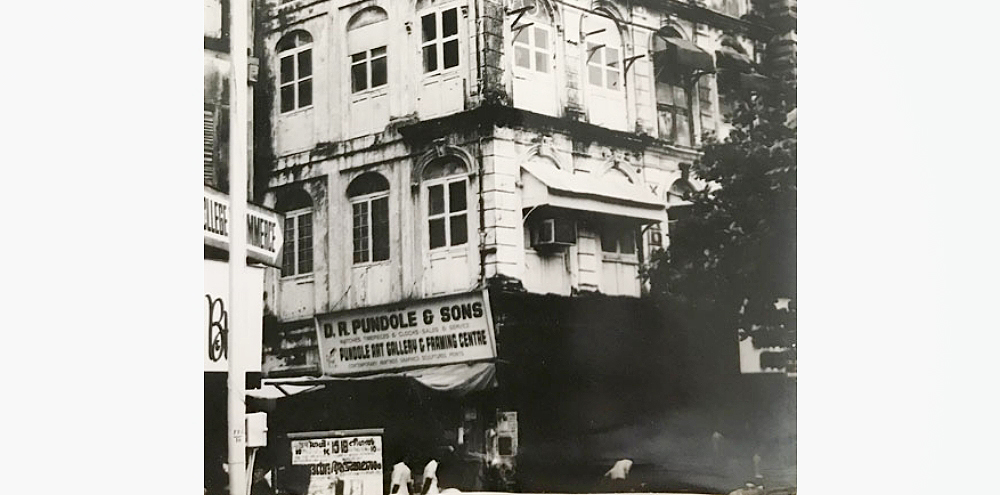 A section of a building facade and a signboard with the English text, ‘D.R. Pundole & Sons, Pundole Art Gallery and Framing Centre’.