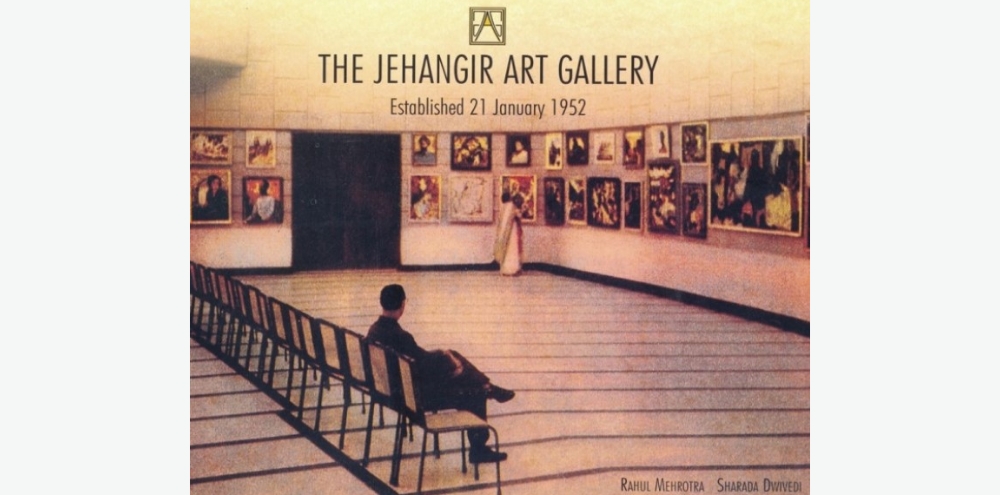 An exhibition hall with chairs and artworks hung on the wall titled 'The Jehangir Art Gallery, Established 21 January 1952’ in English.