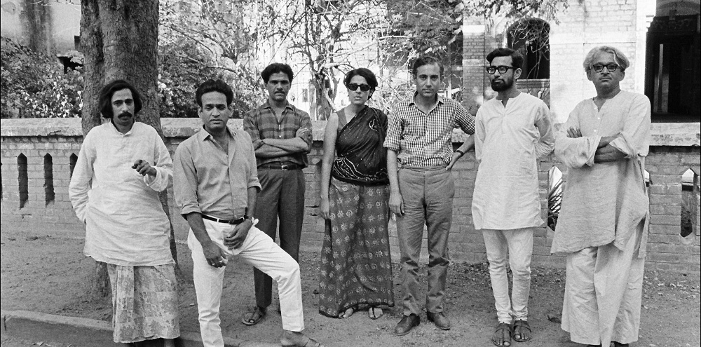 A group of men and a woman stand in a line next to a tree while posing for the camera.