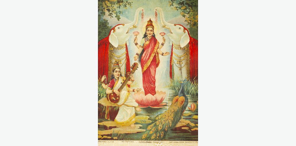 A four-armed woman dressed in a red saree holds lotuses in two of her hands. She stands on a large lotus in a pond with two ornately jewelled white elephants showering flowers on her. In the foreground, a woman wearing a white saree plays the veena next to a peacock.