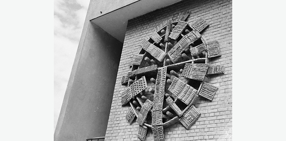 A circular relief mural with patterned panels on the brick facade of a building.