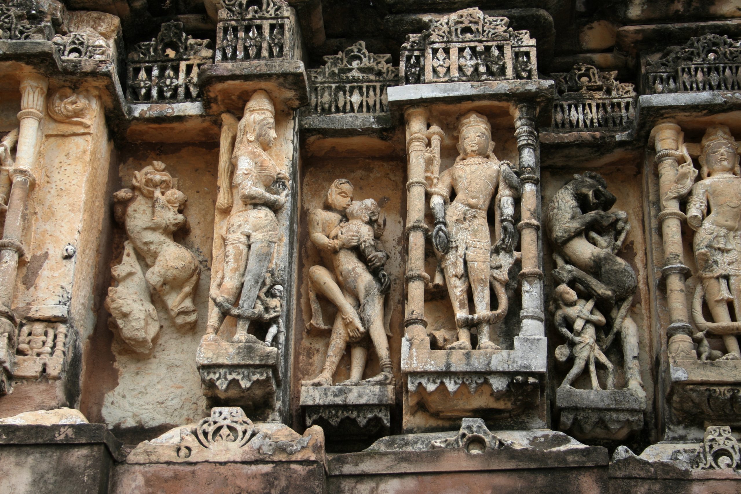 Stone carvings of deities and figures in an embrace on niches and projections of a wall.
