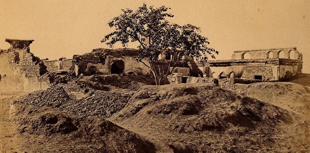 A tree stands in front of building ruins with rubble and mud in the foreground.