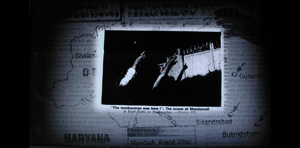 A video still featuring superimposed images of a newspaper, a map of Delhi and a photograph.
