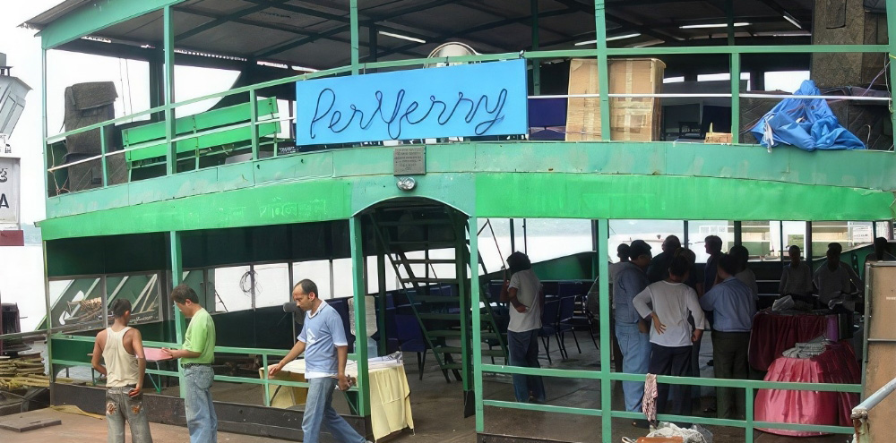 The exterior of a green ferry with the English signboard, ‘Perriferry’ with a scattered group of people in the boat.