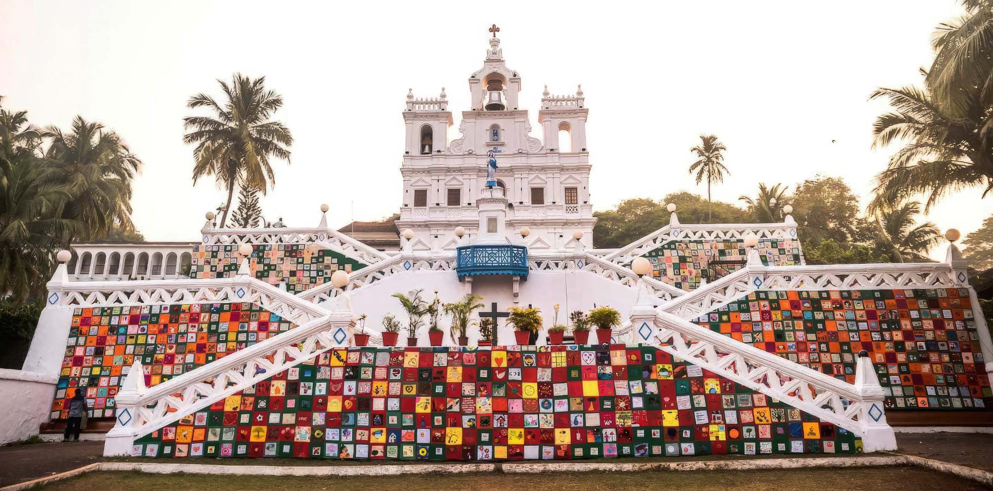 The front facade of a white church building is covered on different levels with a quilt made up of small colourful fabric squares.