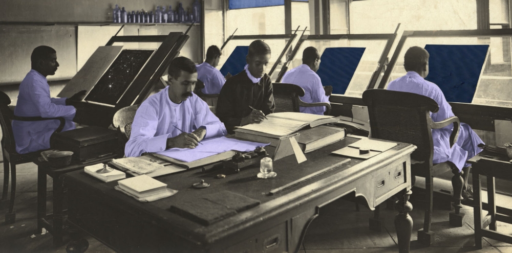 An altered black and white photograph of a group of men working at desks wearing white garments and a few bottles shelved in the background highlighted with a blue tint.