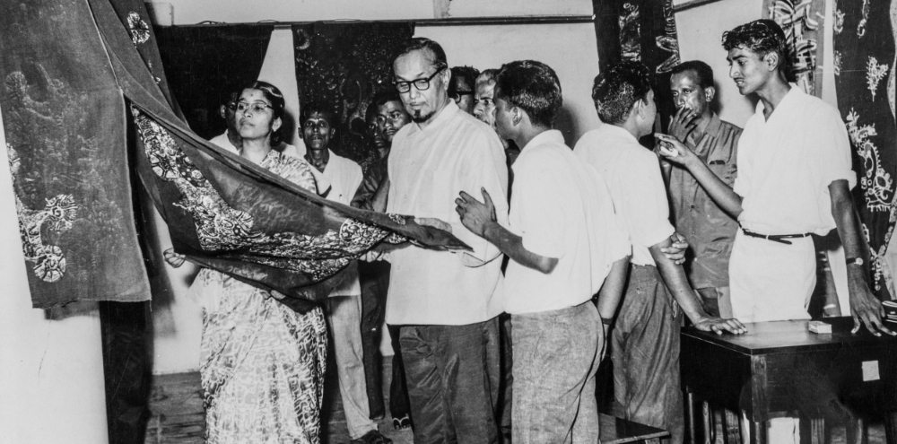 A group of people are deep in discussion as they observe a textile in a room decorated with textiles.