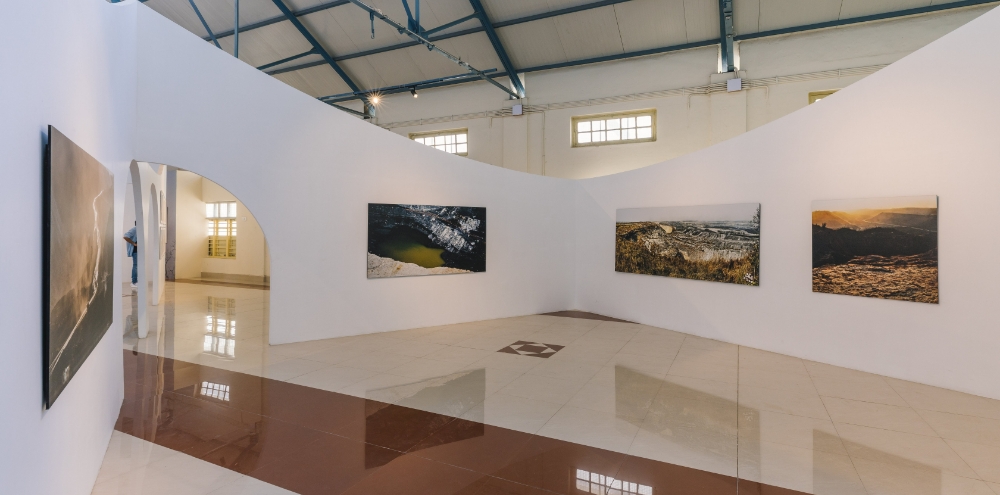 Photographic prints are displayed on white curved walls in a large exhibition space.