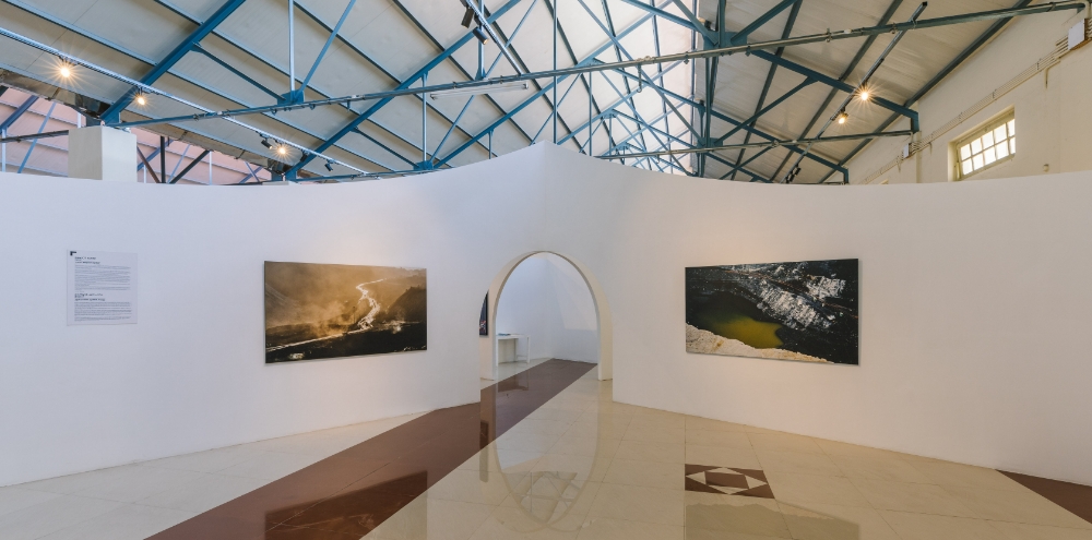 Photographic prints are displayed on white curved walls sectioned by arched doorways in a large exhibition space.