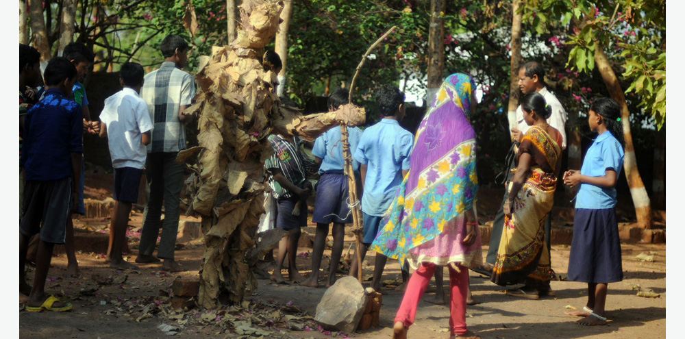 A group of men, women and children walk in the midst of trees.