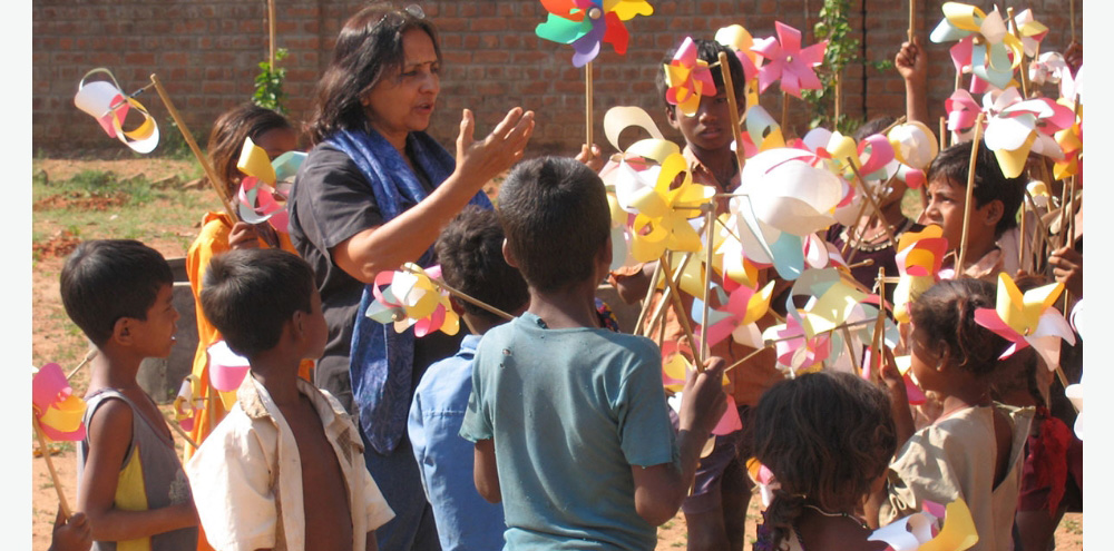 A woman engages in conversation with a group of children holding pinwheels.