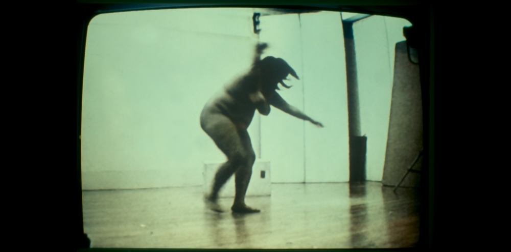 A nude woman spinning on a wooden floor.