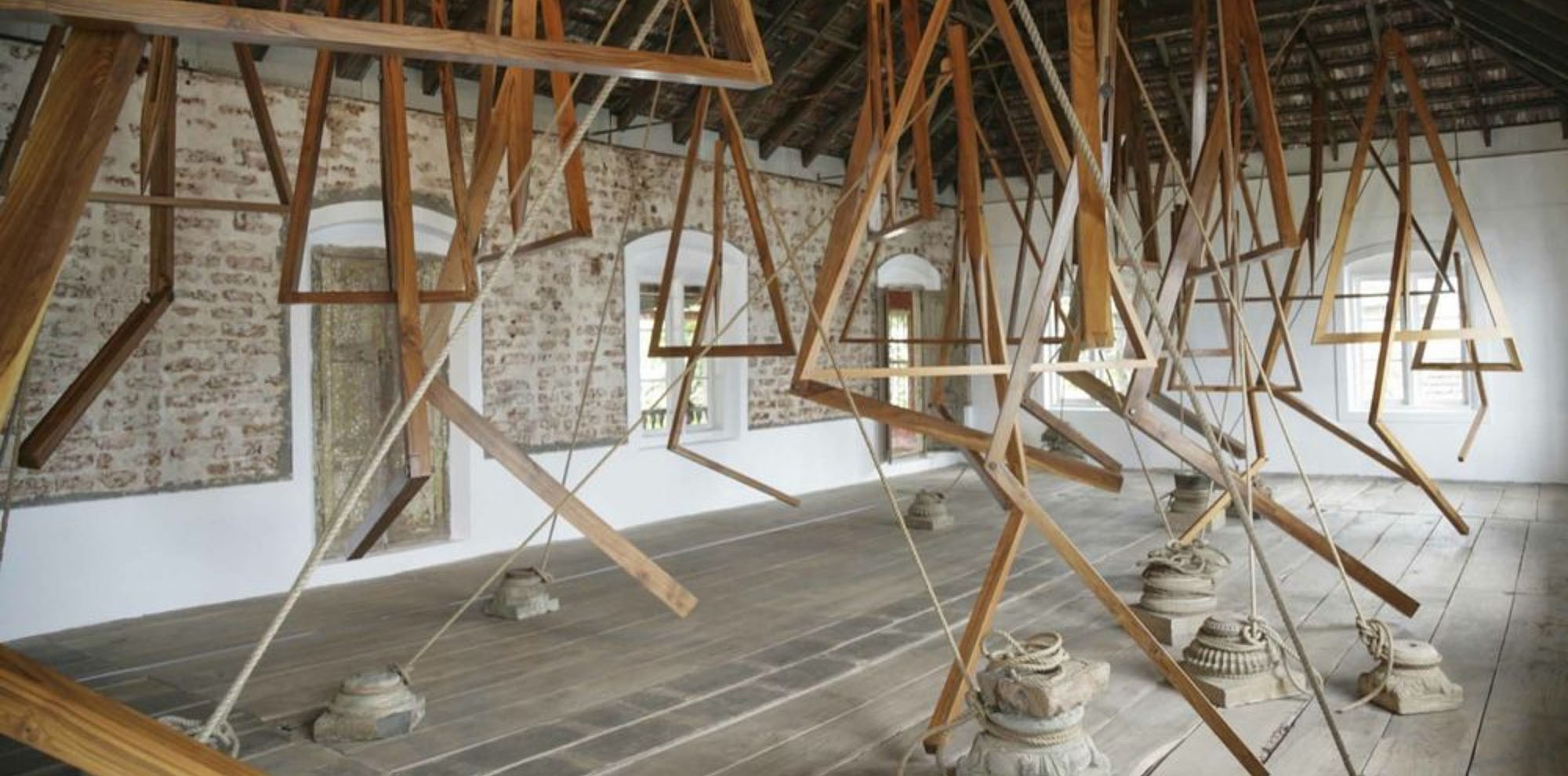 Several wooden structures tied to column bases using ropes are installed in a large exposed brick room.