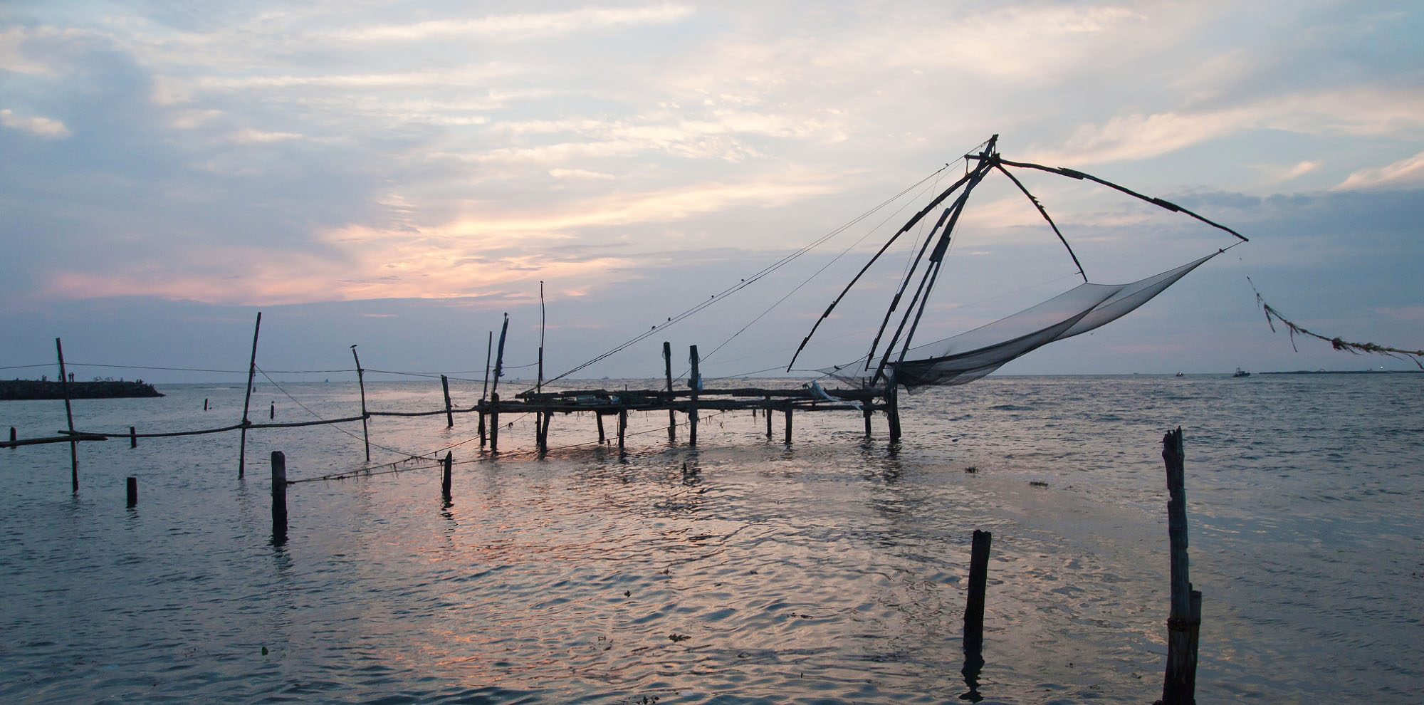 Fishing nets supported by wooden poles in the water with the sun setting in the background.