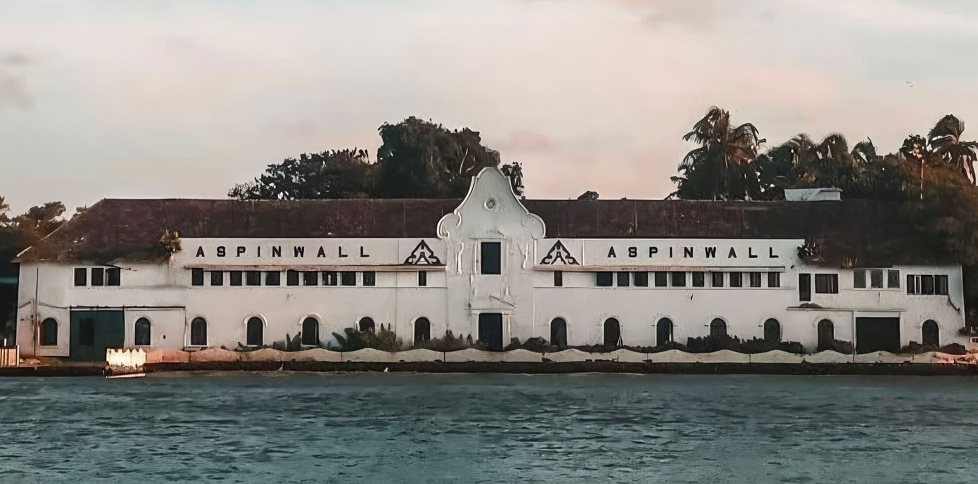 A sea-facing white building with a sloping roof and the English text ‘Aspinwall’ on the front facade.