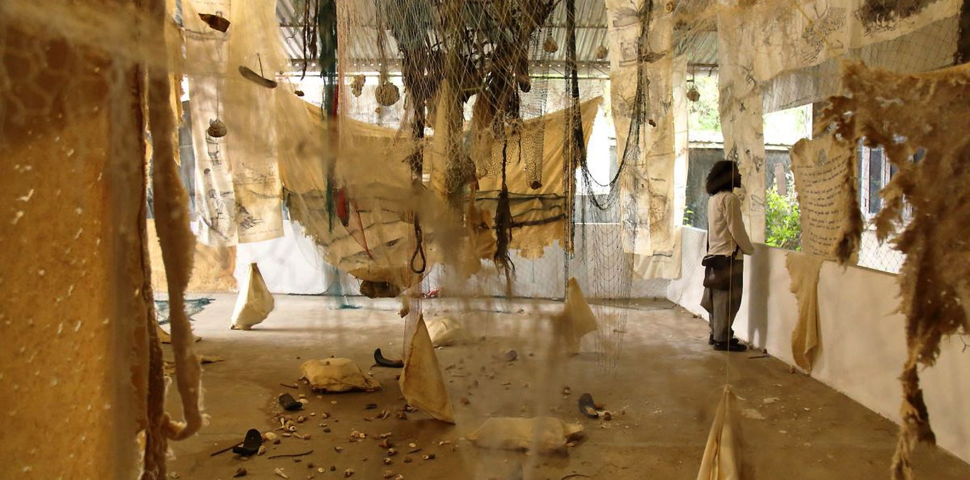 A cluster of hanging cloth, fishnets and sacks arranged chaotically on an open balcony with a man on the right.