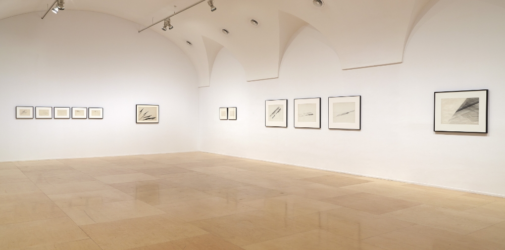 An exhibition space with arched ceilings; multiple sets of black and white framed artworks displayed on white walls.