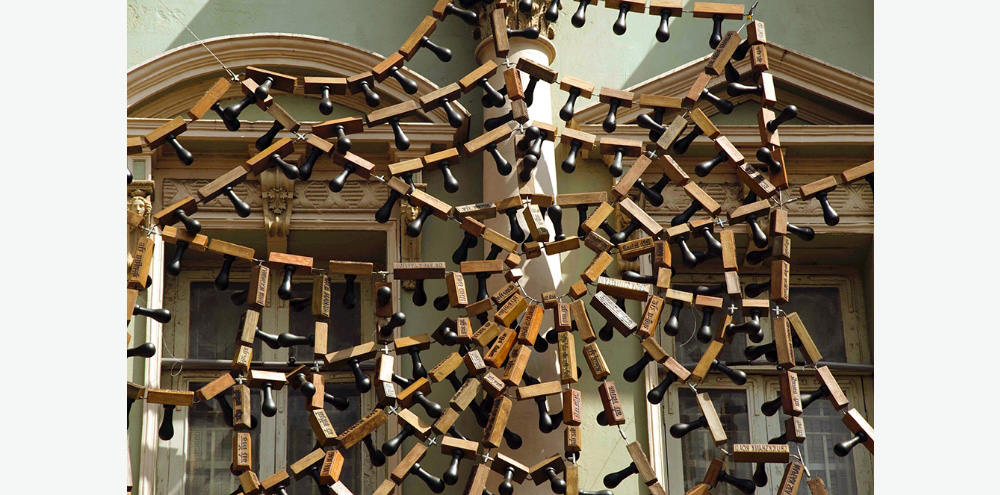 Rubber stamps strung together by a steel rope arranged in a cobweb-like manner on the facade of a blue building.