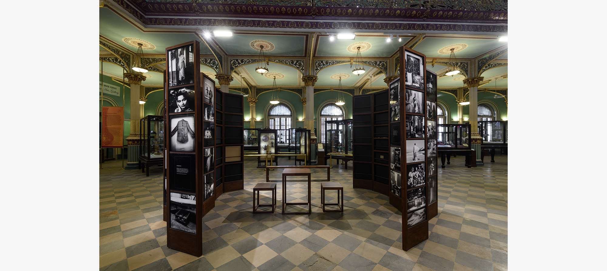 A circular space with a table and two benches surrounded by two wooden folding screens with photographs on either side.