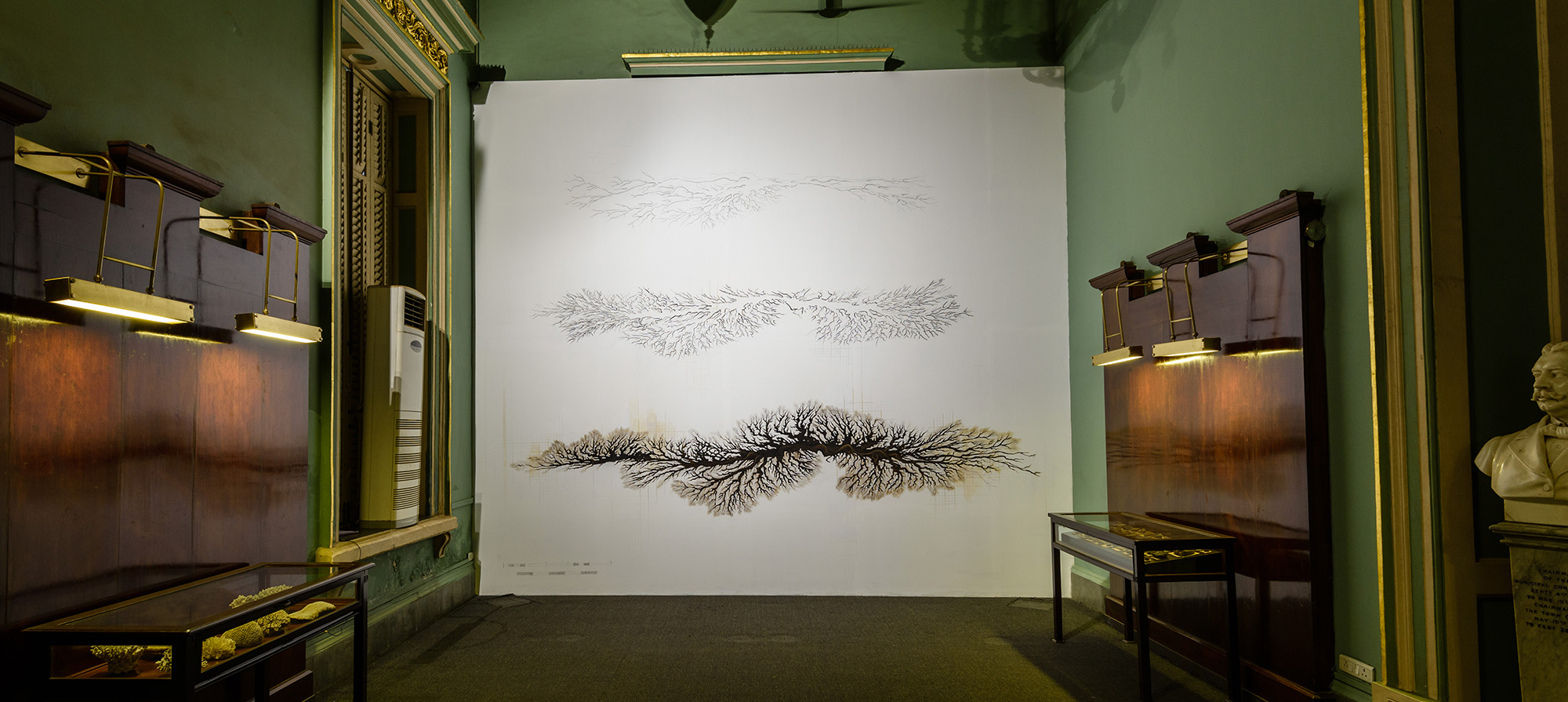 A large vein-like drawing is installed in a green room with two wooden and glass cabinets on either side.